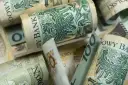 Zwijane banknoty 100 zł, symbolizujące wsparcie finansowe, jak zasiłek rodzicielski, dla młodych rodzin.