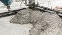 Beton wylewany z betoniarki na podłoże z drobnego kruszywa. Widać formę do wylewania betonu i masę, która tworzy kopiec.