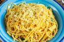 Porcja spaghetti z tartym serem i ziołami w niebieskiej misce.