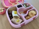 Różowy lunchbox z pysznym, zdrowym śniadaniem do szkoły: wrap z kurczakiem, suszone jabłka, kiwi, orzechy i czekoladowe kuleczki.