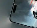 Telefon z ekranem gry Call of Duty Warzone Mobile. Widać spadające postacie z czerwonymi smugami dymu na tle burzowych chmur.