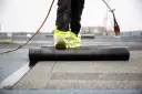 Pracownik na dachu z palnikiem, rozwijający papę podkładową.