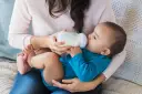 Mama karmi dziecko butelką. To przykład karmienia mieszanego, gdzie dziecko otrzymuje zarówno mleko matki, jak i mleko modyfikowane.