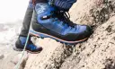 Close-up of a blue and black hiking boot with orange accents, gripping a rocky surface.