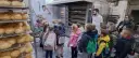 Dzieci z plecakami oglądają piec piekarniczy i półki z chlebem.