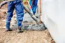 Pracownicy wylewają beton na zbrojenie. Sprawdź aktualną suchy beton cena 1m3.