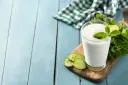 Szklanka białego napoju, idealna na kefir w ciąży, ozdobiona plasterkami ogórka i miętą.