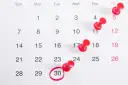 Kalendarz z zaznaczonym 30 dniem miesiąca. Ile godzin pracy to pełny etat w miesiącu? Czerwone pinezki oznaczają ważne daty.