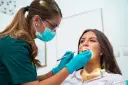 Dentystka w masce i rękawiczkach bada zęby pacjentki. To nie jest wyrywanie 8, ale rutynowa kontrola.