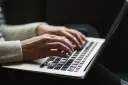 Dłonie piszą na laptopie. Ktoś przygotowuje wypowiedzenie umowy o pracę po angielsku, szukając wzoru.