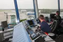 Kontroler ruchu lotniczego, mimo młodego wieku, skupiony na monitorach. Widok na lotnisko i samoloty.
