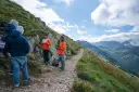 Grupa turystów na szlaku w Tatrach, dyskutująca o tym, ile się schodzi z Kasprowego Wierchu. W tle piękne, górskie krajobrazy.