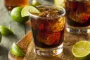Orzeźwiający Cuba Libre, czyli rum z colą i limonką, z kostkami lodu i świeżymi ćwiartkami cytrusów na drewnianym blacie.