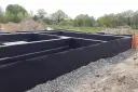 Fundament domu z czarną izolacją przeciwwilgociową i drenażową, otoczony żwirem.