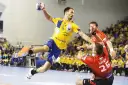 Piłkarz ręczny Telekom Veszprem w żółtej koszulce skacze do rzutu, broniony przez zawodnika w czerwonej.