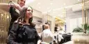Friseurin stylt lächelnde Kundin mit Lockenstab in modernem Salon.