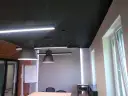 Nowoczesne biuro z czarnym sufitem (RAL 9004), wiszącymi lampami i ceglaną ścianą.