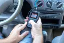 Ręce trzymające skaner diagnostyczny, który pokazuje menu z opcją "02 Sensor Test". To narzędzie pomoże zdiagnozować problemy z czujnikiem spalania stukowego.