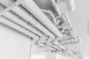 Skomplikowany system białych rur, przypominający pex, biegnie pod sufitem, tworząc geometryczny wzór.