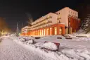 Zimowy wieczór w sanatorium godnym polecenia. Ośnieżone ławki i oświetlony budynek zapraszają do odpoczynku.