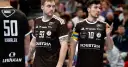 Dwóch zawodników w brązowych koszulkach, jeden z numerem 93, drugi z numerem 10. Luka Cindrić, kapitan z opaską na ramieniu, rozmawia z kolegą z drużyny.