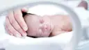 Delikatna dłoń otula głowę śpiącego wcześniaka.