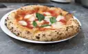 Pizza Margherita na białym talerzu, z widocznym puszystym brzegiem i świeżą bazylią.