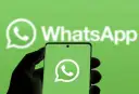 Hand hält Smartphone mit WhatsApp-Logo vor grünem Hintergrund.