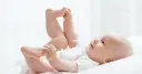 Uśmiechnięte dziecko leży na plecach, podnosząc nóżki. Czas na zmianę pampersów na większe, gdy maluch rośnie.