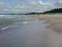 Plaża z falującym morzem i osobą w czerwonej bluzie na piasku.