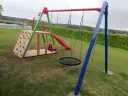 Plac zabaw z wspinaczką, zjeżdżalnią, huśtawkami i okrągłą huśtawką.