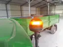 Pomarańczowa lampa ostrzegawcza na wysięgniku, przy zielonym ciągniku i przyczepie.