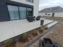 Nowy taras betonowy z meblami ogrodowymi i młodymi krzewami w przygotowanej rabacie.