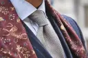 Elegancki mężczyzna w błękitnej koszuli, szarym krawacie i bordowym szalu z motywem jeleni. Całość emanuje nonszalancką elegancją, czyli sprezzaturą.