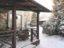 Tani taras na gruncie z wiklinowymi meblami, otoczony ośnieżonymi drzewami. Idealne miejsce na zimową kawę.