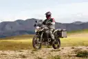 Motocyklista w kasku i stroju podróżuje na motocyklu BMW 800 GS po piaszczystej drodze, w tle górzysty krajobraz.