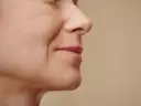 Zbliżenie na twarz kobiety, widoczne subtelne bruzdy nosowo wargowe, podkreślające naturalne piękno.