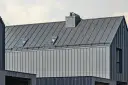 Nowoczesny dach z blachy na rąbek, z oknami połaciowymi i kominem. Sprawdź blacha na rąbek cena m2.