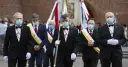 Rycerze Kolumba w garniturach i maskach maszerują z flagą.