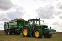 Zielony traktor John Deere z przyczepą wypełnioną ziemniakami na polu.