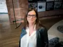 Małgorzata Szczęśniak w okularach i czarnej ramonesce, zamyślona.