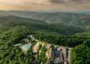Widok z lotu ptaka na hotel SPA z basenem i zjeżdżalnią, otoczony lasem i górami.