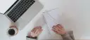 Ręce piszą CV po niemiecku przy laptopie, notatniku i kawie.