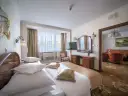 Elegancki pokój hotelowy z dużym łóżkiem, toaletką i widokiem na salon. Dowiedz się, ile kosztuje noc w hotelu Gołębiewski.