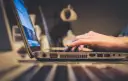 Dłoń pisząca na klawiaturze laptopa, widok z boku.