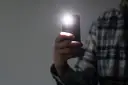 Dłoń trzyma smartfon z włączoną latarką.
