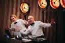Dwóch DJ-ów w białych koszulach i czarnych muszkach, z uśmiechem na twarzy, przygotowuje się do imprezy. Zastanawiasz się, ile bierze DJ za wesele?