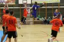Mateusz Orłowski w skoku do rzutu w meczu piłki ręcznej. Zawodnik w niebieskiej koszulce z numerem 9 celuje do bramki, podczas gdy jego przeciwnicy w pomarańczowych strojach próbują go zatrzymać.