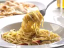 Porcja spaghetti z ziołami na widelcu, w tle płaski chleb.