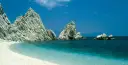 White pebble beach with turquoise water and dramatic white rock formations under a clear blue sky.
